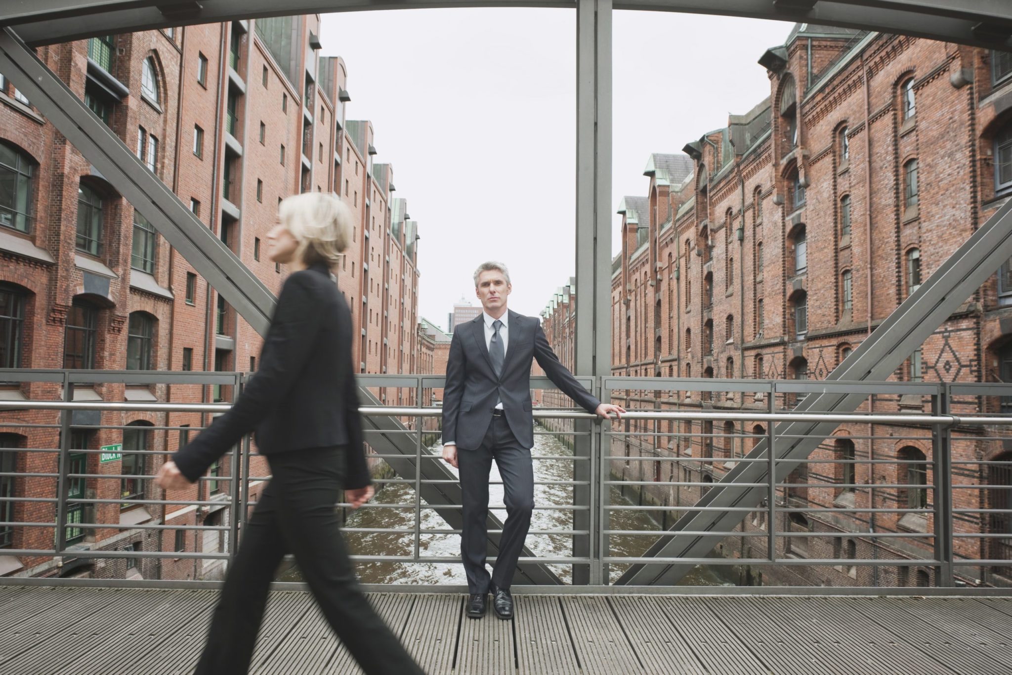 Germany, Hamburg, Businesswoman crossing bridge, Businessman in background leaning against railing