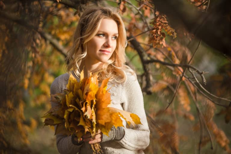 Herbstliche Fotosessions mit LET IT CLICK - Blondhaarige Frau hält gelbe Blätter in den Händen, umgeben von warmen Herbsttönen.