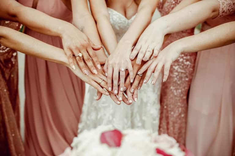 JGA planen: Braut und Brautjungfern in rosa Kleidern, die ihre Hände ausstrecken