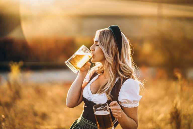 Junge Frau in bayerischer Tracht genießt Bier auf dem Oktoberfest inmitten eines malerischen Feldes