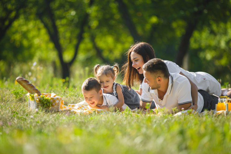 Eine Familie liegt beim Picknick auf der Wiese und zeigt glückliche Gesichter. Familienporträts von LET IT CLICK fangen solche besonderen Momente ein.