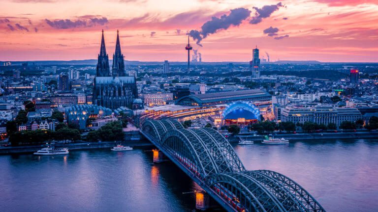 Köln bei Sonnenuntergang - Die Kölner Brücke mit dem Dom im warmen Abendlicht auf einem beeindruckenden Foto. Buche hier einen Fotografen.