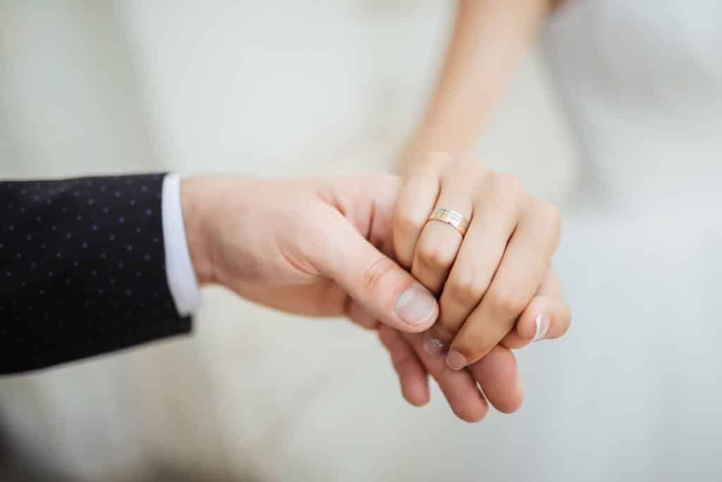 Unvergessliche Hochzeitsmomente: Hände des frisch vermählten Paares mit Eheringen, festgehalten von LET IT CLICK Fotografen
