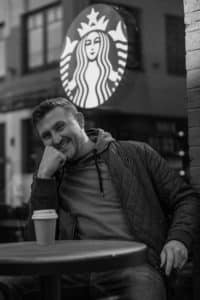 Lebensfreude festgehalten: Das Porträt fängt die Lebensfreude und positive Ausstrahlung des Mannes ein, während er vor einem bekannten Café sitzt.