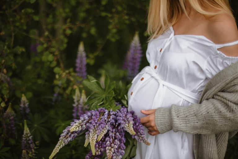 Schwangerschaftsfotografie: Frau in weißem Kleid mit Blumenstrauß.