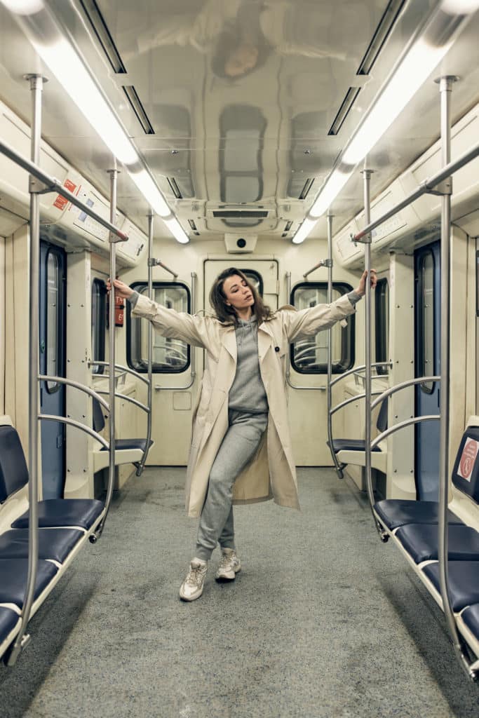 A girl in a beige trench coat rides in a subway car.