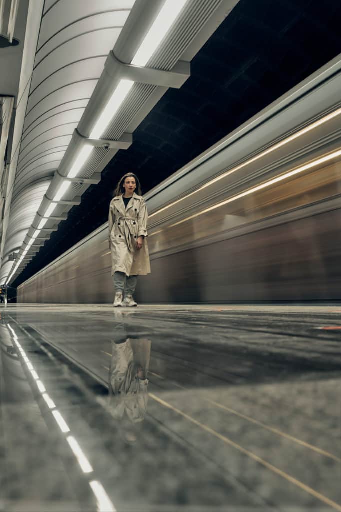 Girl in a beige trench coat in the subway waiting for the train.