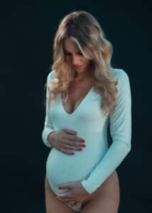 Strahlende werdende Mutter in heller Beleuchtung, hält liebevoll ihren Babybauch und lächelt glücklich während des Fotoshootings.