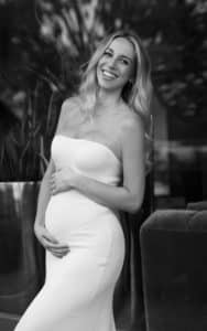 Eindrucksvolles Schwarz-Weiß-Bild einer glücklichen schwangeren Frau, die während eines Fotoshootings sanft ihren Babybauch umfasst und lächelt.