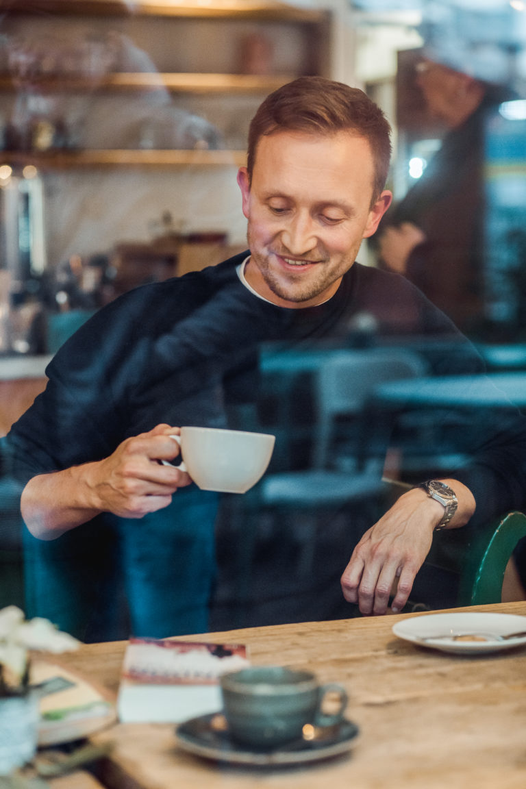 Ein lächelnder Mann genießt einen Kaffee in einem Porträtfoto, das Freude und Entspannung ausstrahlt.