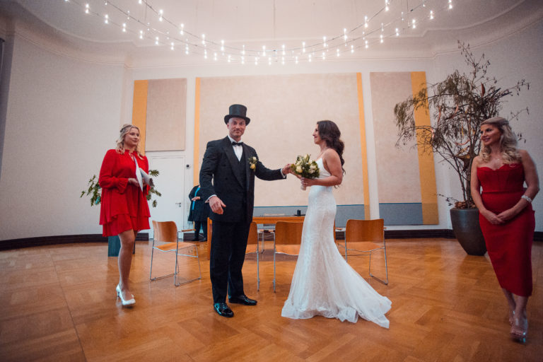 Ein bezaubernder Anblick. Im Saal in Münster halten Braut und Bräutigam glücklich Hand in Hand, während ein warmes Licht den Raum erhellt und das Fotoshooting verschönert. Dieses Bild fängt die tiefe Verbundenheit und das strahlende Glück des Paares perfekt ein., Standesamt, Münster,