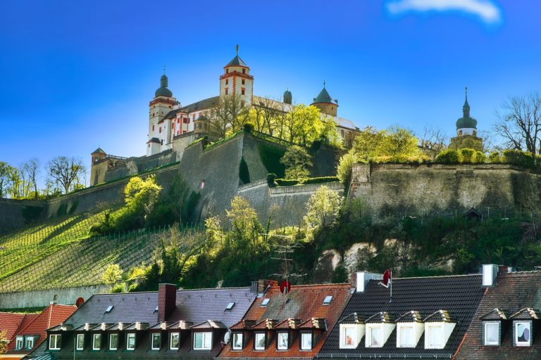 Die Festung Marienberg erhebt sich majestätisch über Würzburg, umgeben von dichten Bäumen, mit charmanten Wohnhäusern, die sich am Fuß der Festung entlangziehen.