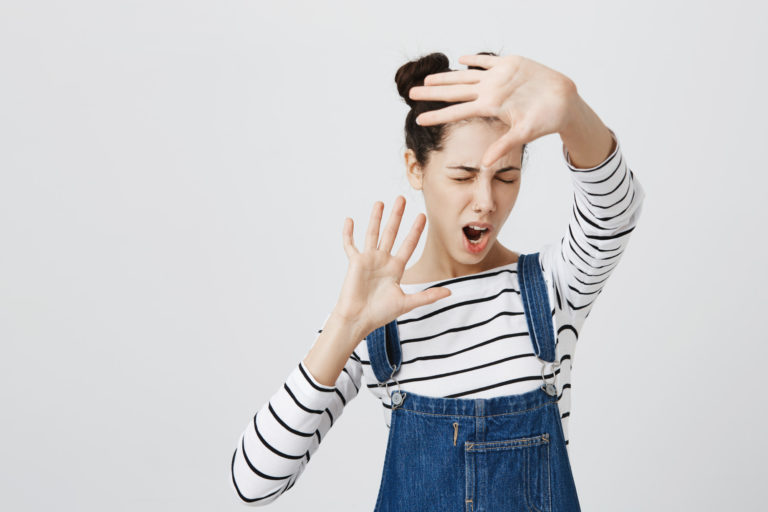 Junge Frau zeigt typische Anzeichen von Kameraangst, indem sie das Gesicht abschirmt – ein verbreitetes Problem bei Fotoshootings.