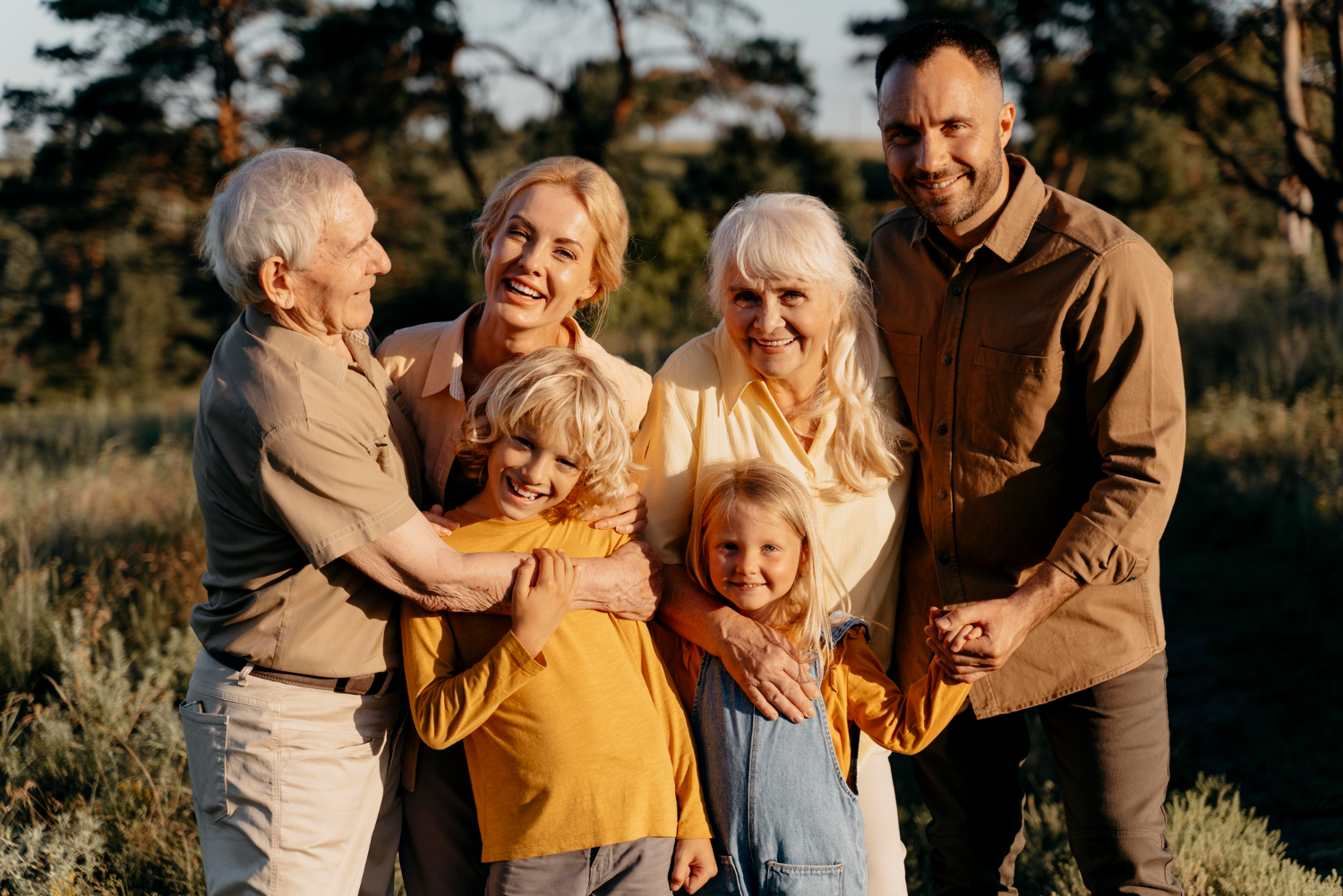 Eine glückliche Familie, bestehend aus Großeltern, Eltern und Kindern, posiert für ein Mehrgenerationen Shooting im Freien bei Sonnenuntergang.