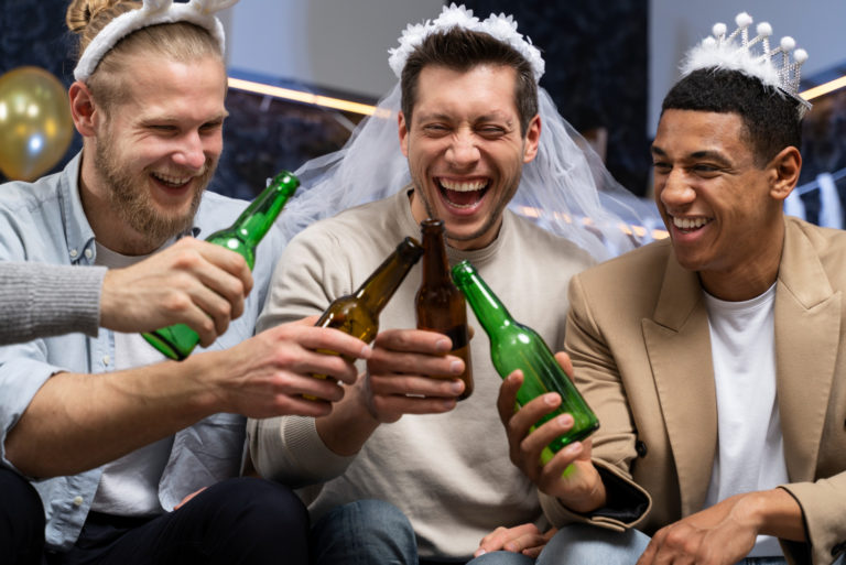 Gruppe von Männern bei einem professionellen JGA-Shooting, lachend und mit Bierflaschen anstoßend; der Bräutigam trägt Schleier und Krone.