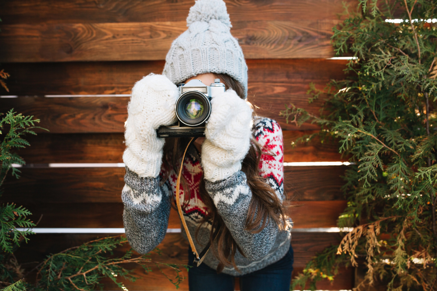 Perfekt für winterliche Fotoshootings ohne Schnee. Frau mit Strickmütze, Winterpullover und Handschuhen hält eine Kamera in der Hand.