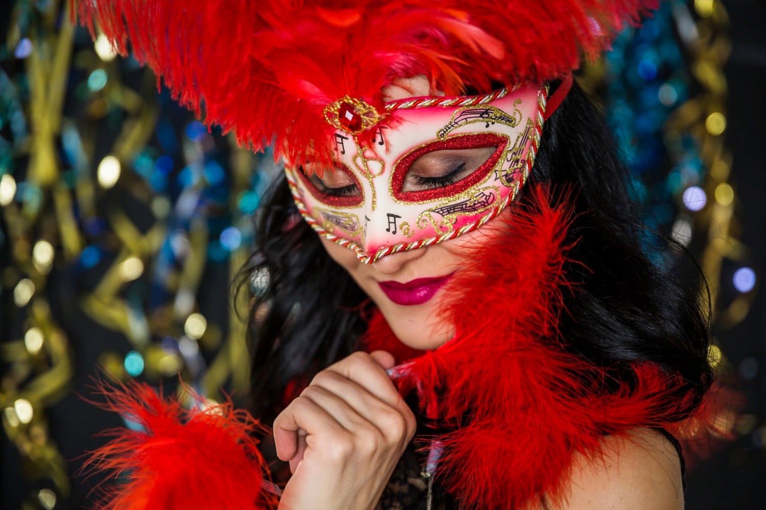 Eine Frau mit einer verzierten roten Maske und Federboa posiert für ein kreatives Karneval-Fotoshooting vor einem schimmernden Hintergrund.